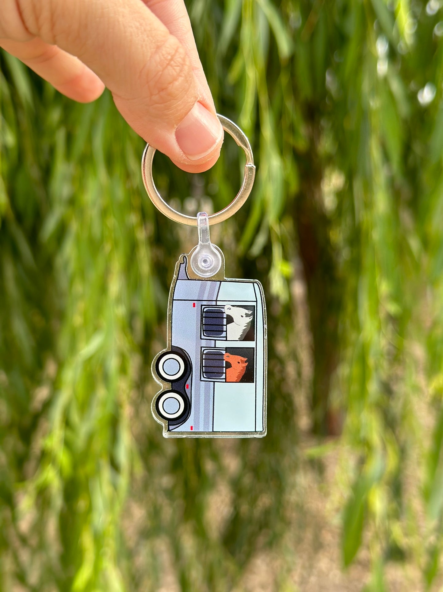 keychain of blue horse trailer with a grey and chestnut horse inside being held in front of a tree