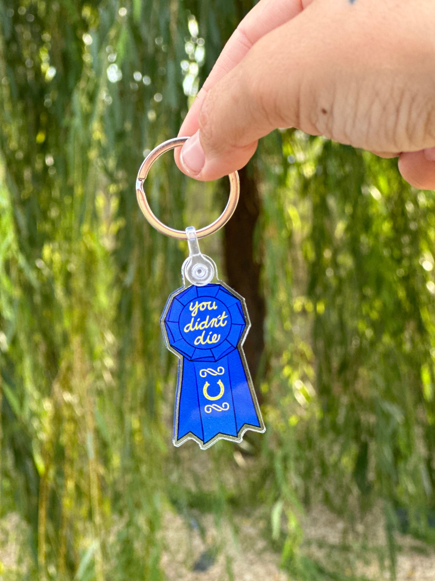 blue horse show ribbon keychain with words "you didn't die" written at top and a horseshoe at the bottom