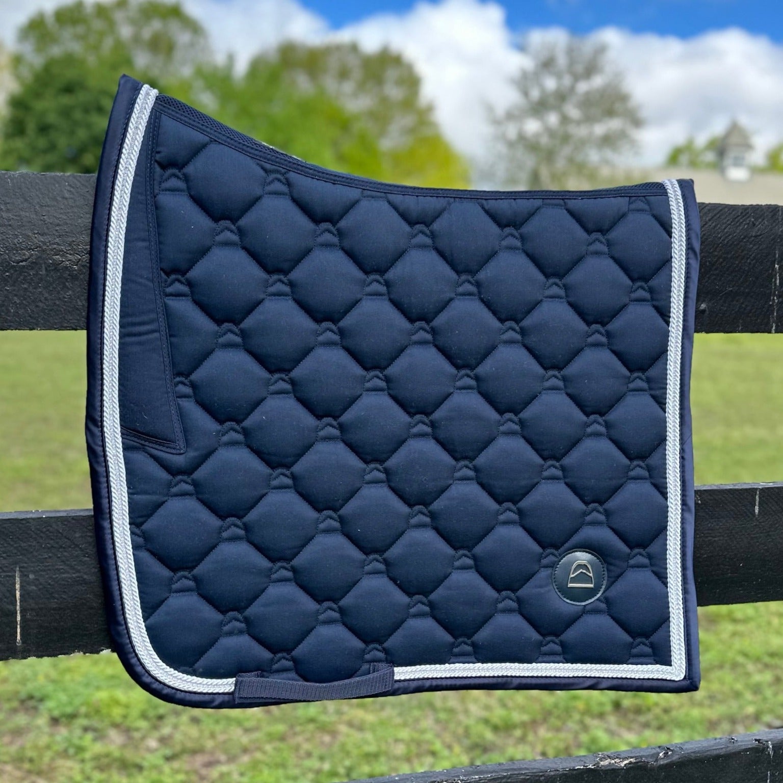 navy dressage saddle pad with white trim and crystal trim on fence in front of horse pasture