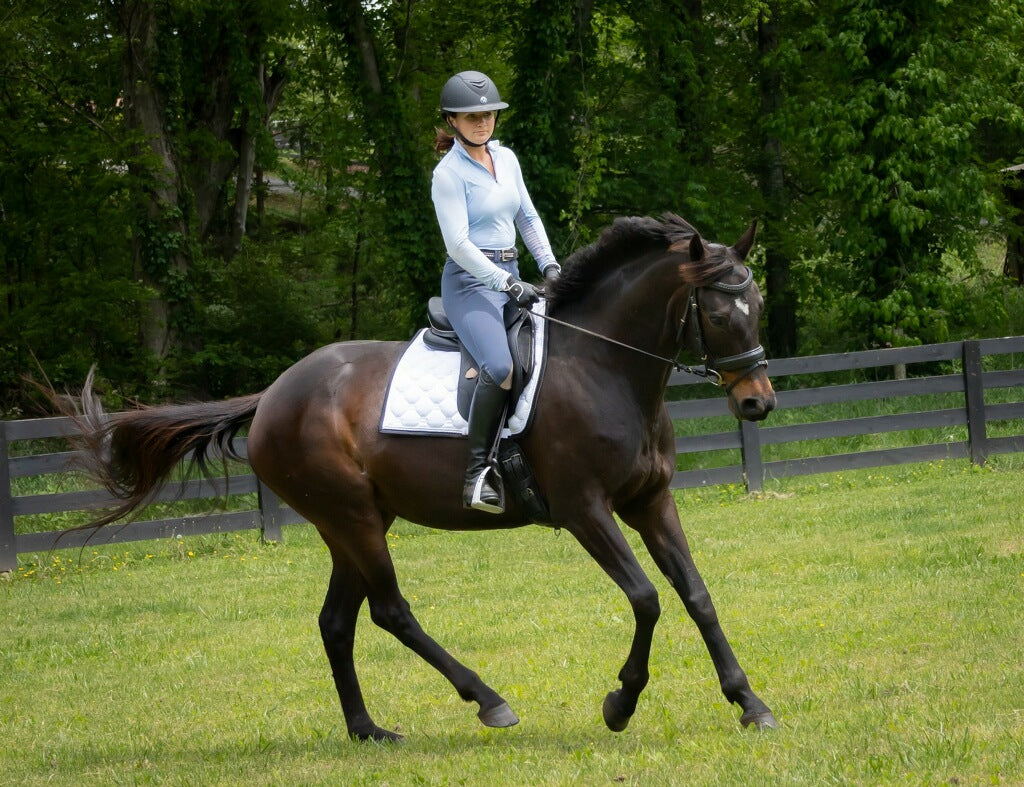 Girl cantering on bay horse in field with white saddle pad and black fence